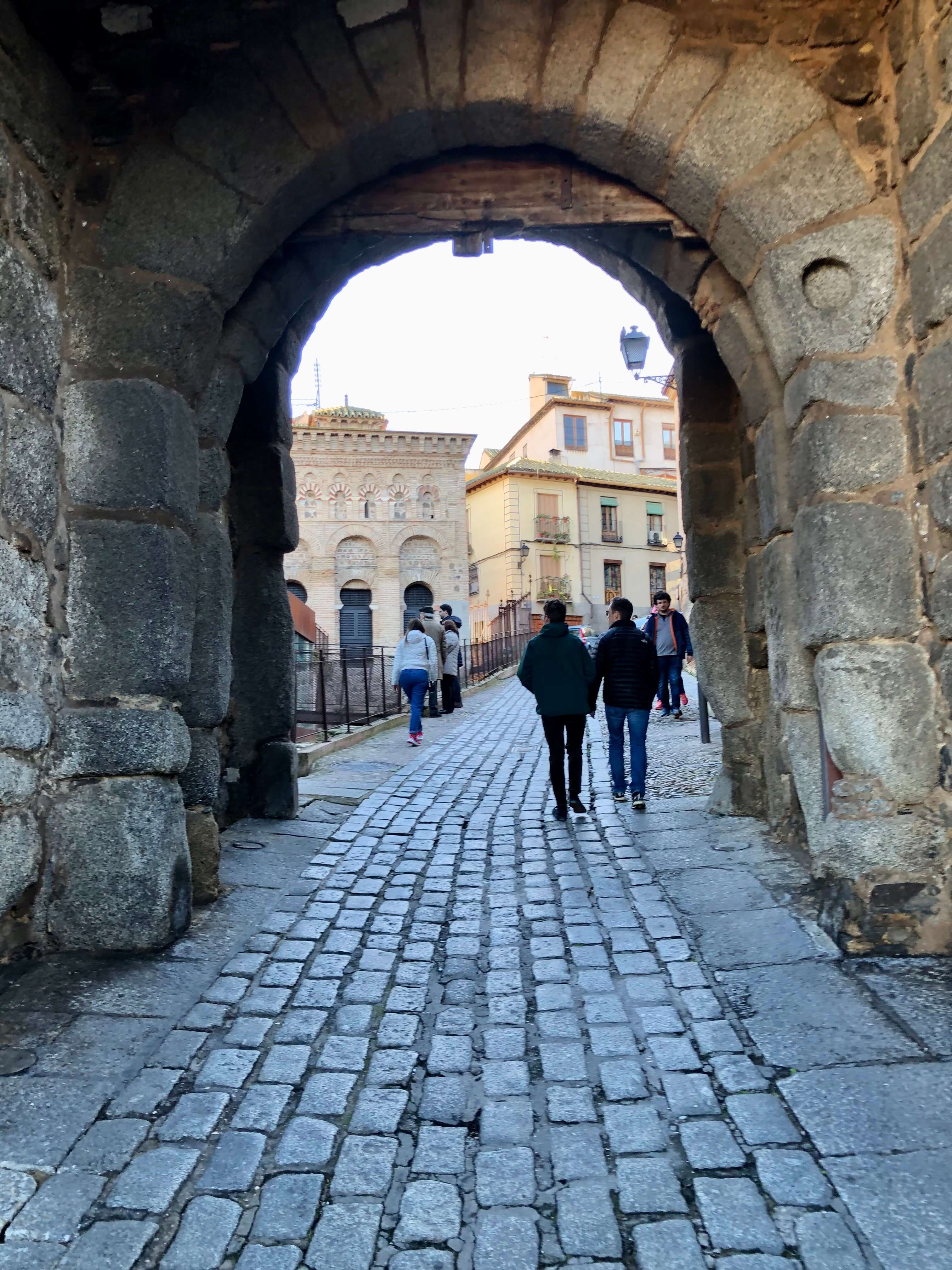 People walking through archway on cobblestone streets in Toledo, Spain